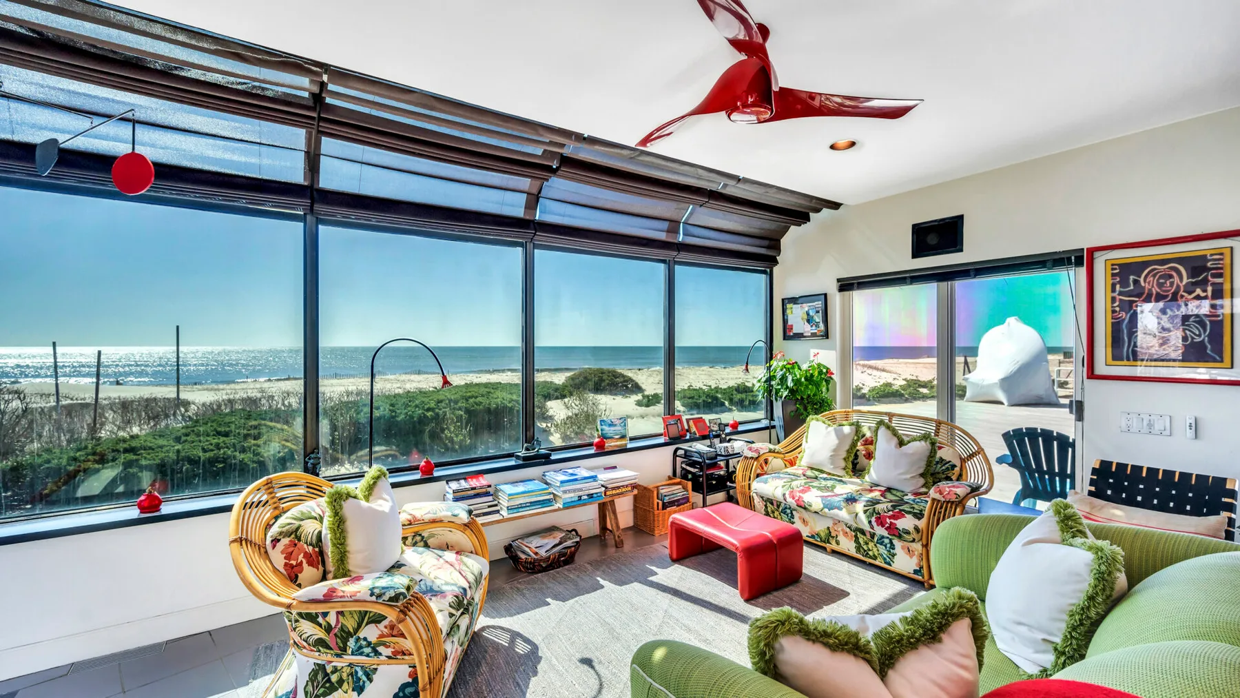 A bright living room with colorful seating beside large windows overlooking the ocean.