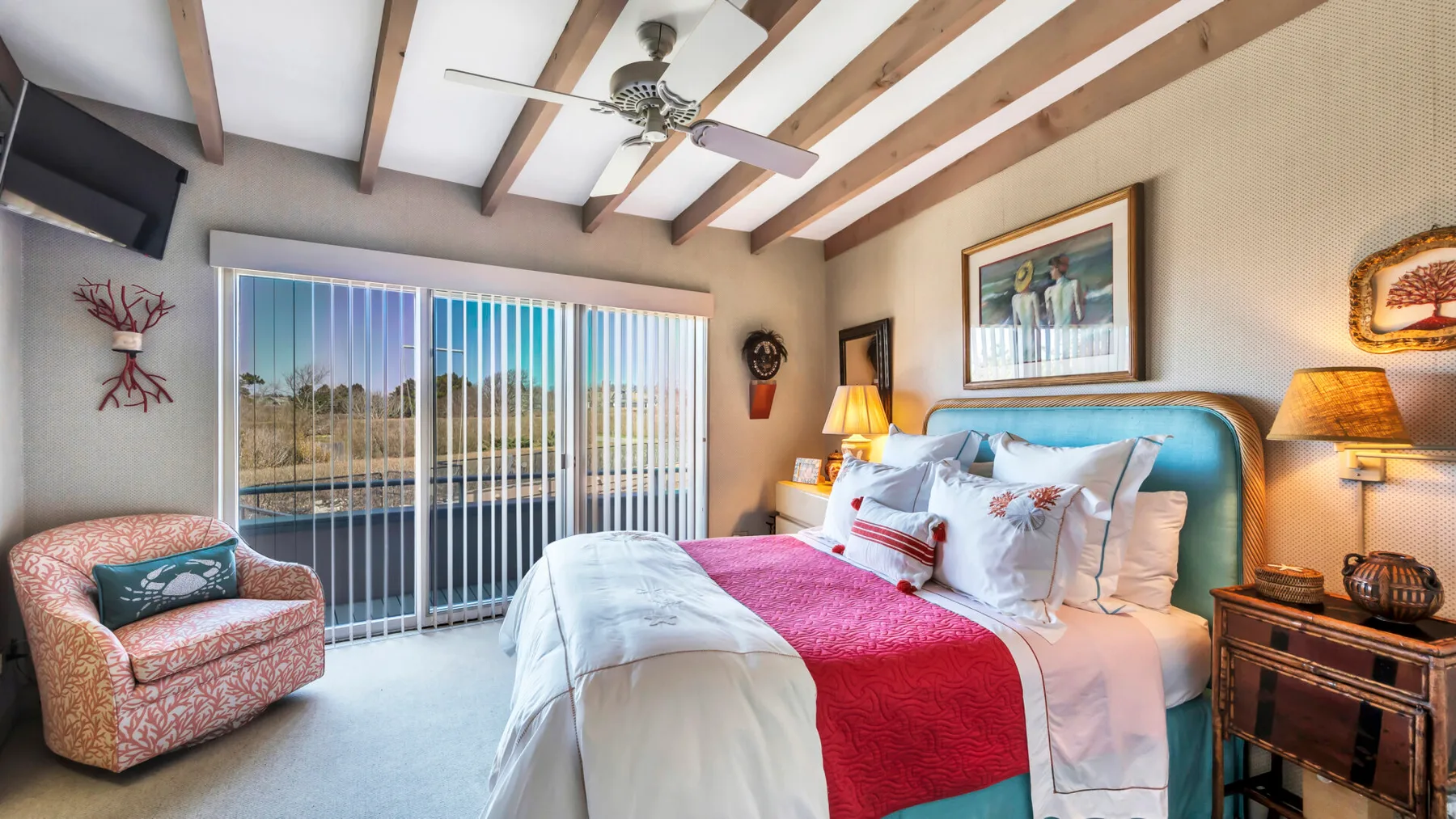A bedroom with a bed, patterned armchair, and sliding glass doors.