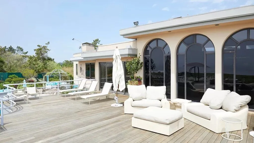 A sunny outdoor terrace with seating and tall arched glass doors.