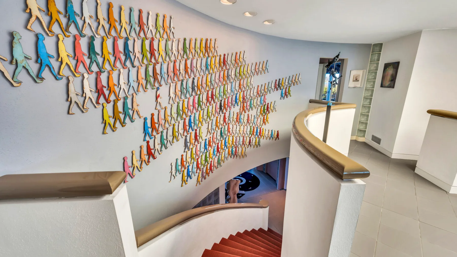 Curved stairwell with red steps and a wall covered in colorful figure decorations.
