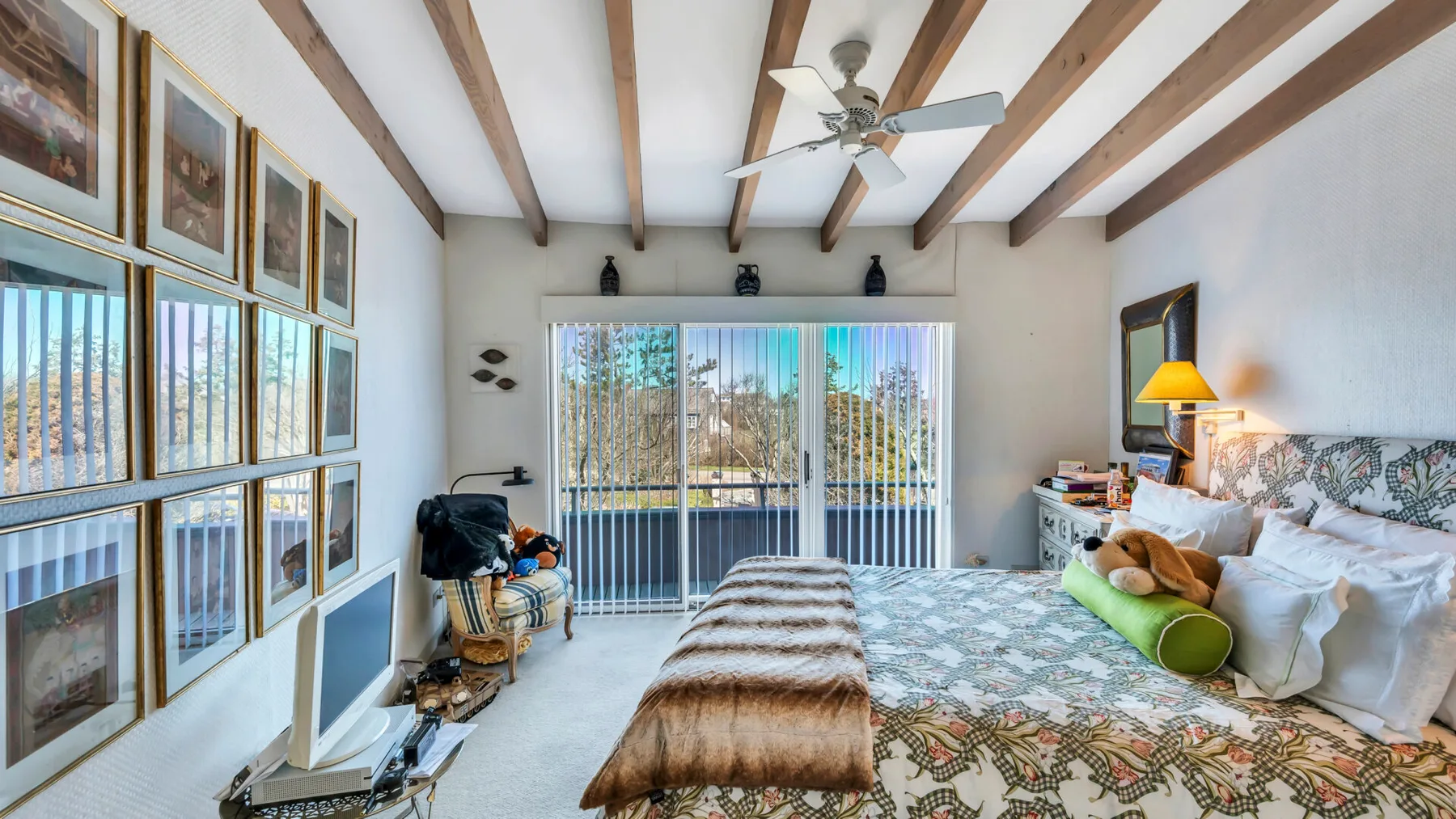 A bedroom with a large bed, framed pictures, and sliding glass doors.