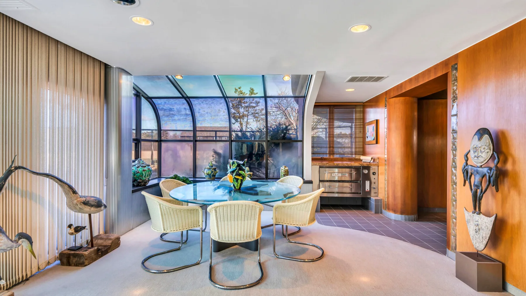 A dining area with a glass table and curved chairs beside floor-to-ceiling windows.