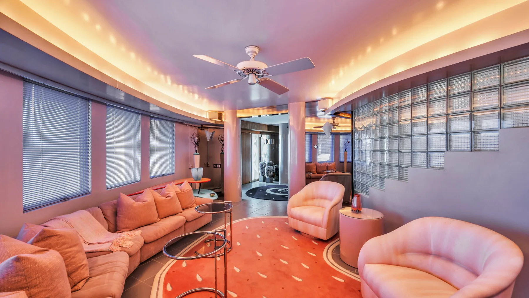 A warmly lit lounge with curved seating, low tables, and large windows.