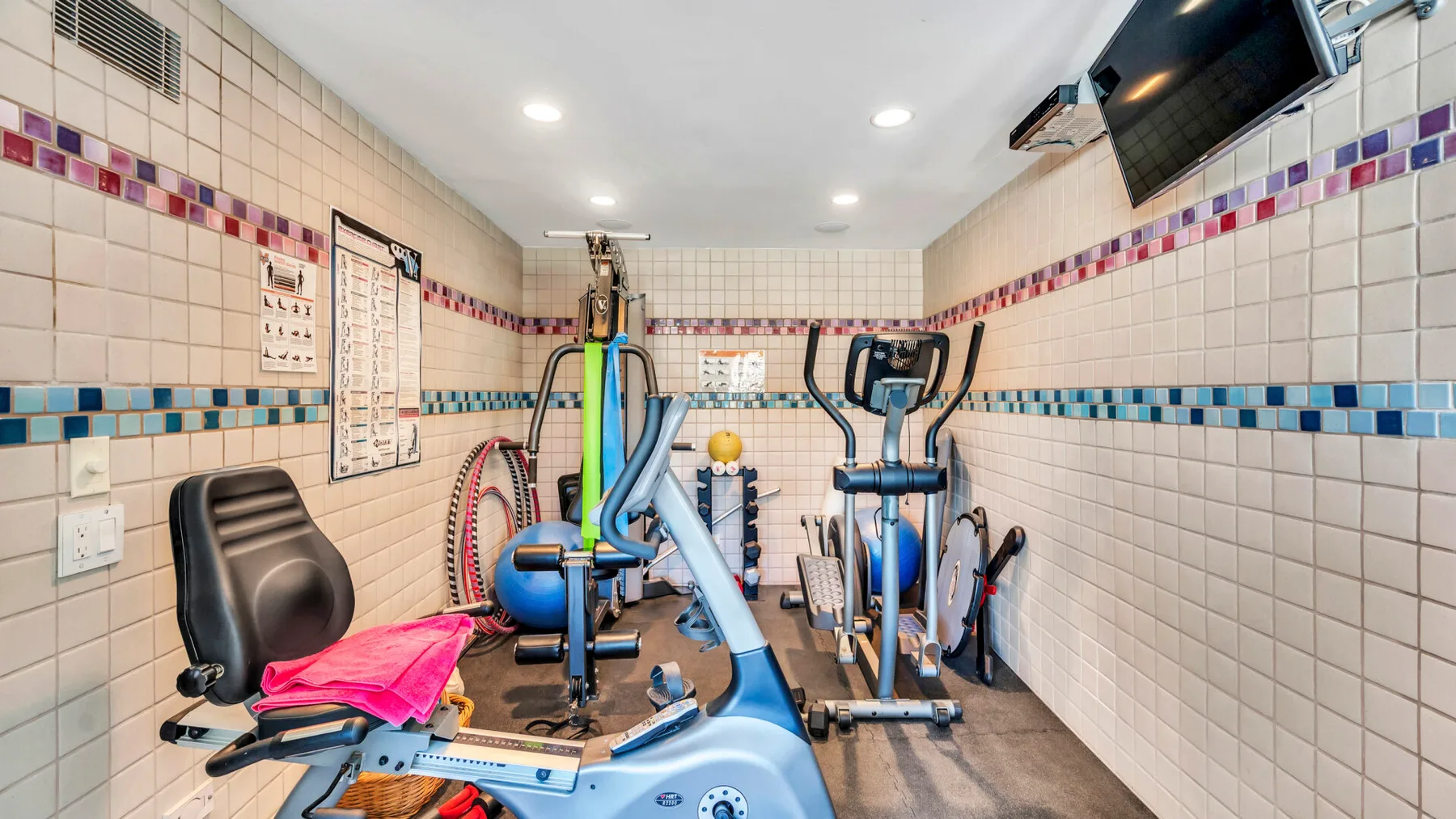 A small exercise room with stationary bikes, weight machines, and tiled walls.
