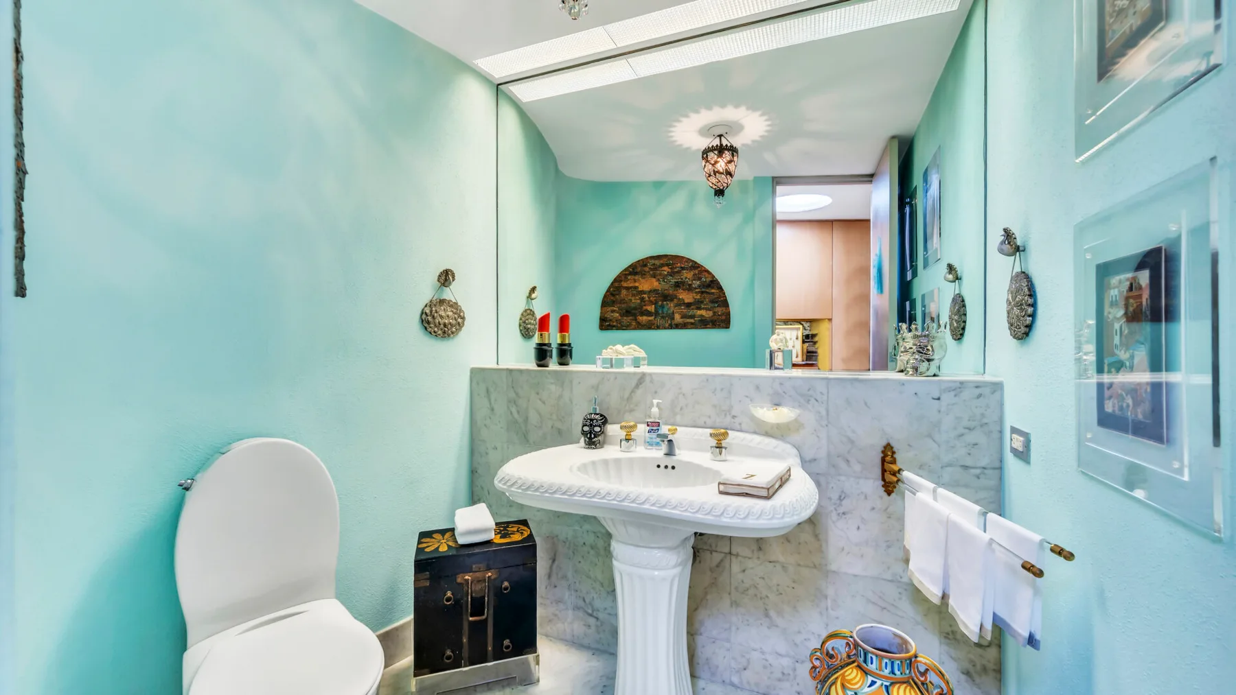 A bright bathroom with a pedestal sink, pale blue walls, and framed pictures.