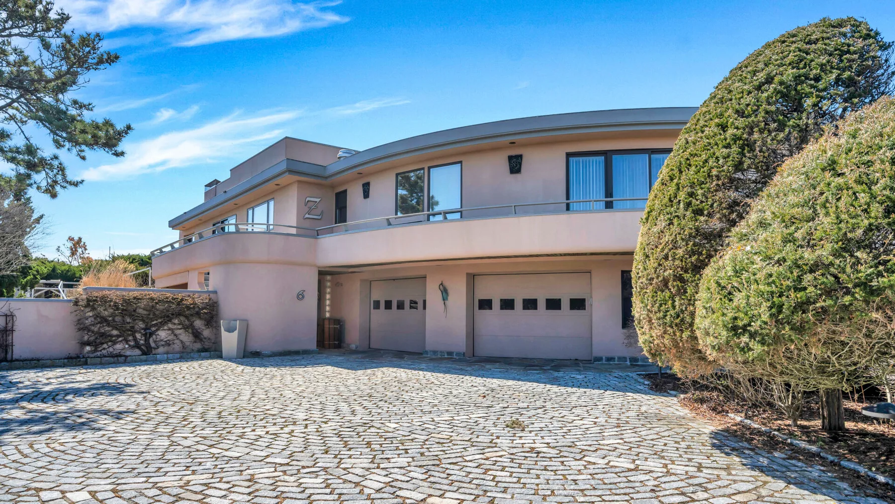 A modern house faces a broad paved driveway, with trimmed hedges along the side.