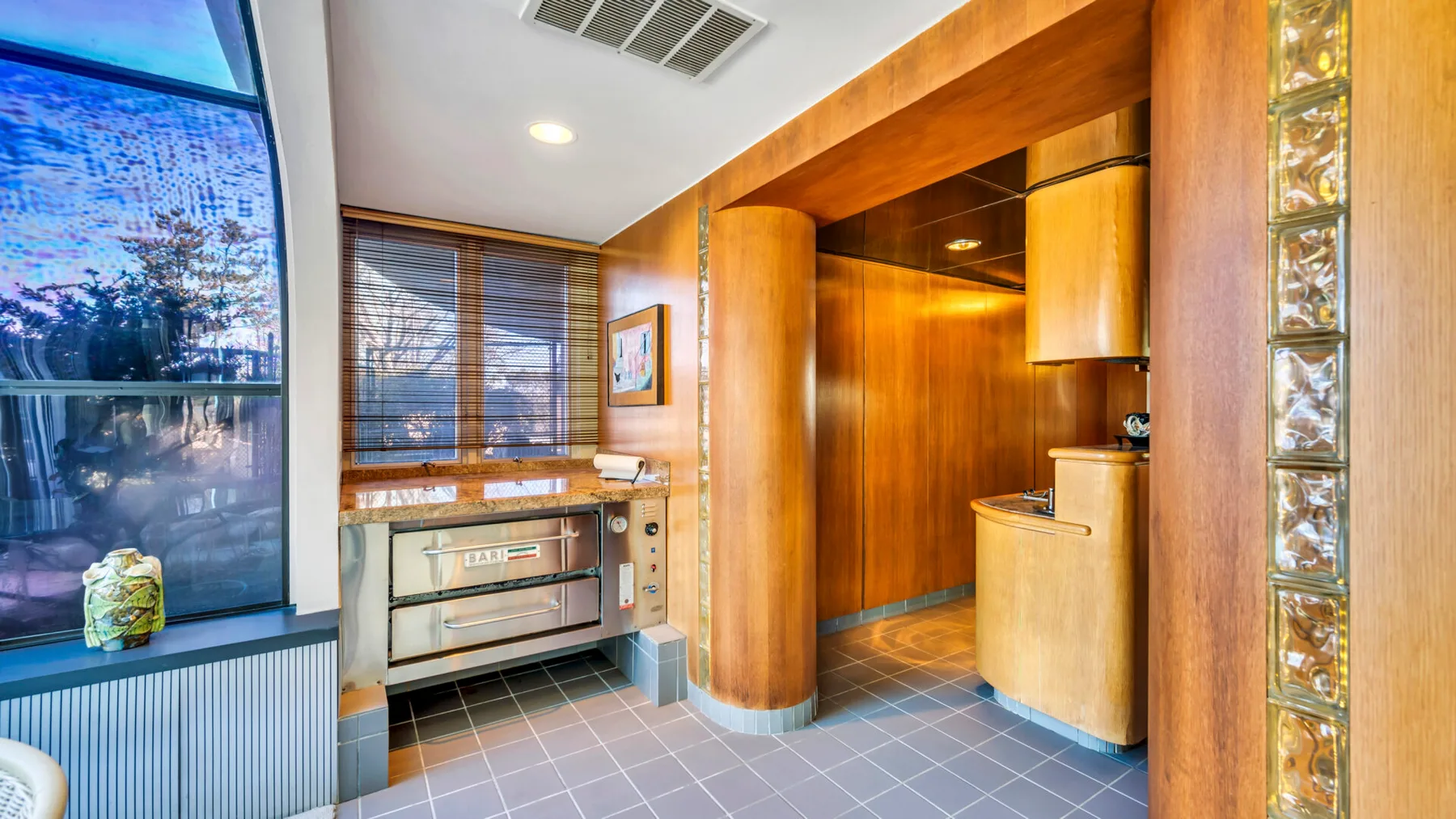 A compact kitchenette with wood cabinetry, a counter, and a large window.