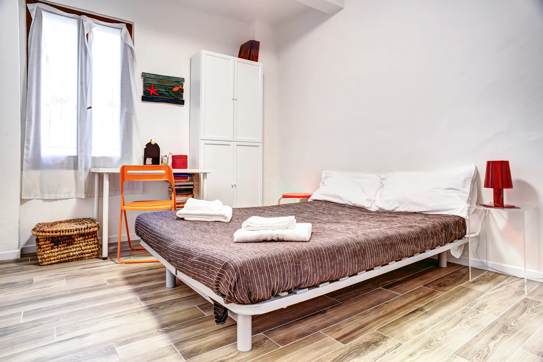 A bedroom with a bed, white wardrobe, and desk beside the window.