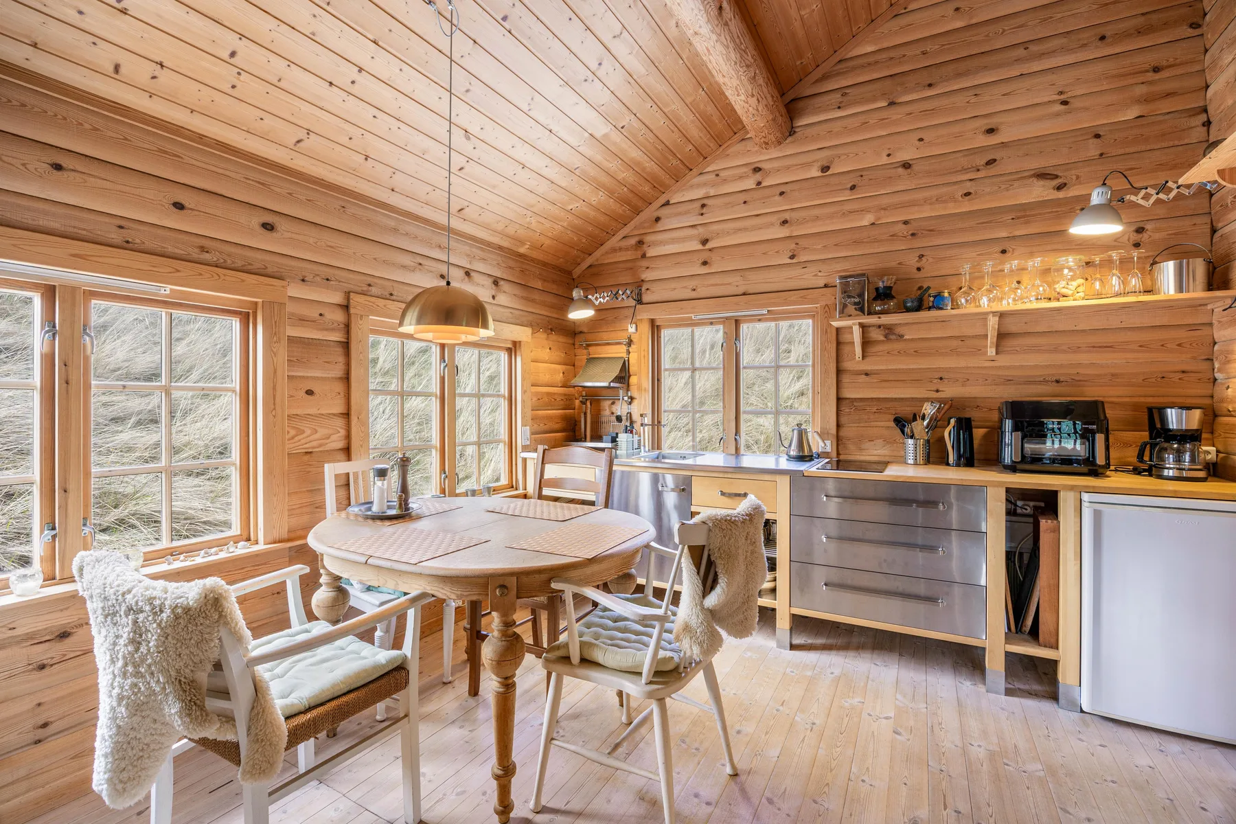 Cocina y comedor revestidos de madera, con una mesa junto a grandes ventanas.