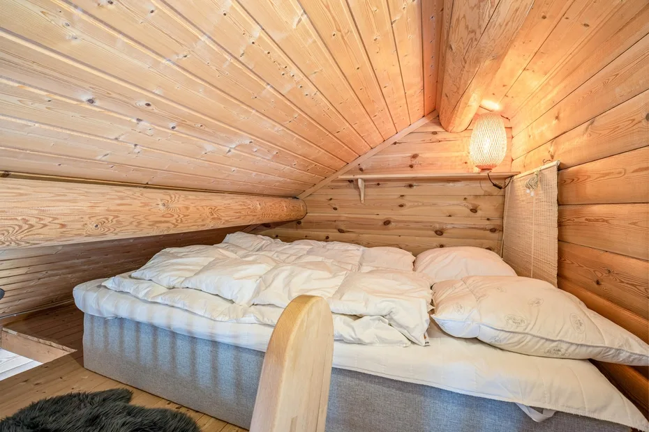 Una cama con ropa de cama blanca está bajo un techo de madera inclinado.