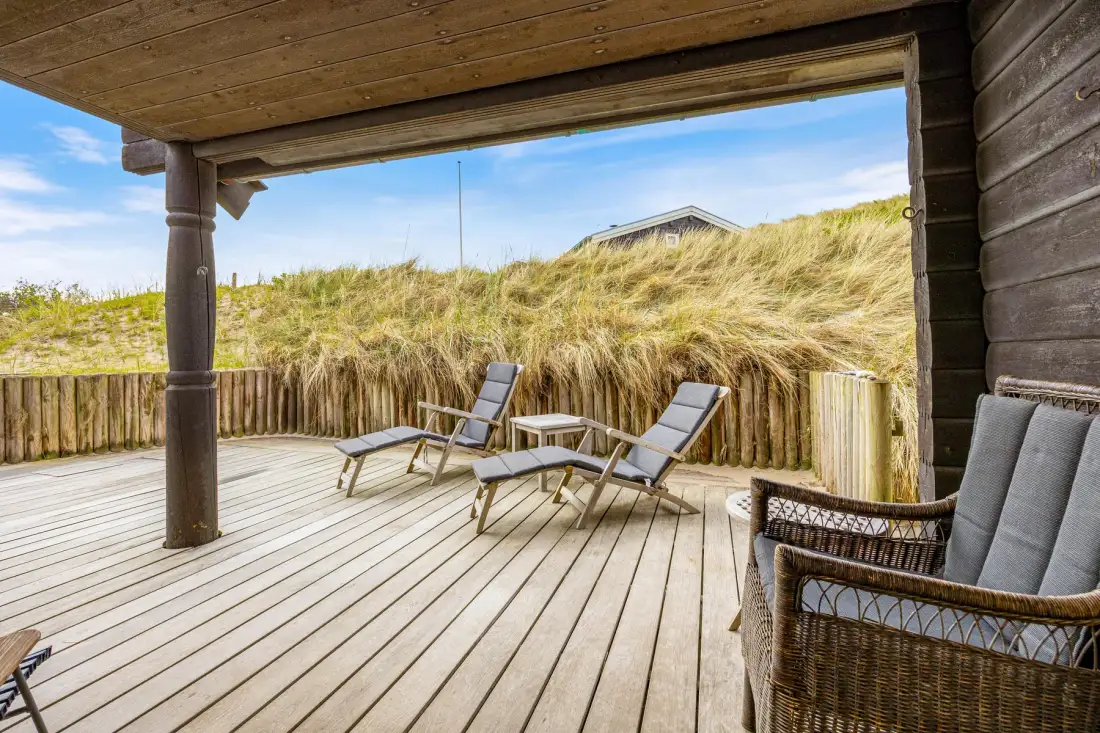 Una terraza de madera cubierta con asientos exteriores da a dunas cubiertas de hierba.