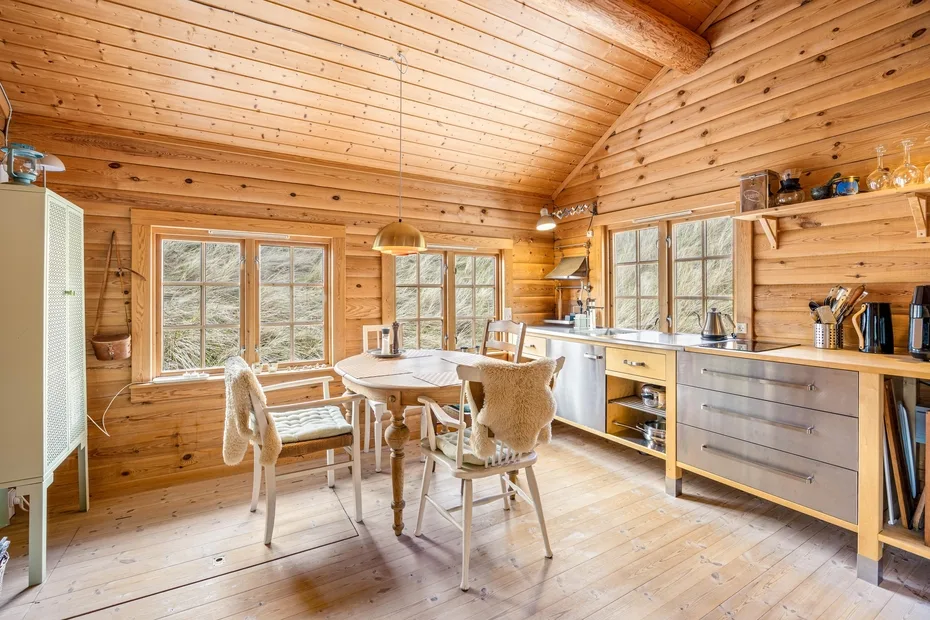 Cocina y comedor revestidos de madera, con una mesa junto a grandes ventanas.