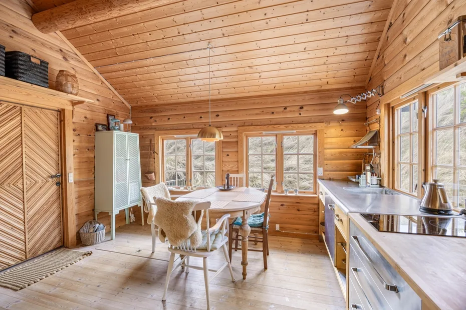 Una cocina y comedor revestidos de madera, con una mesa junto a las ventanas.