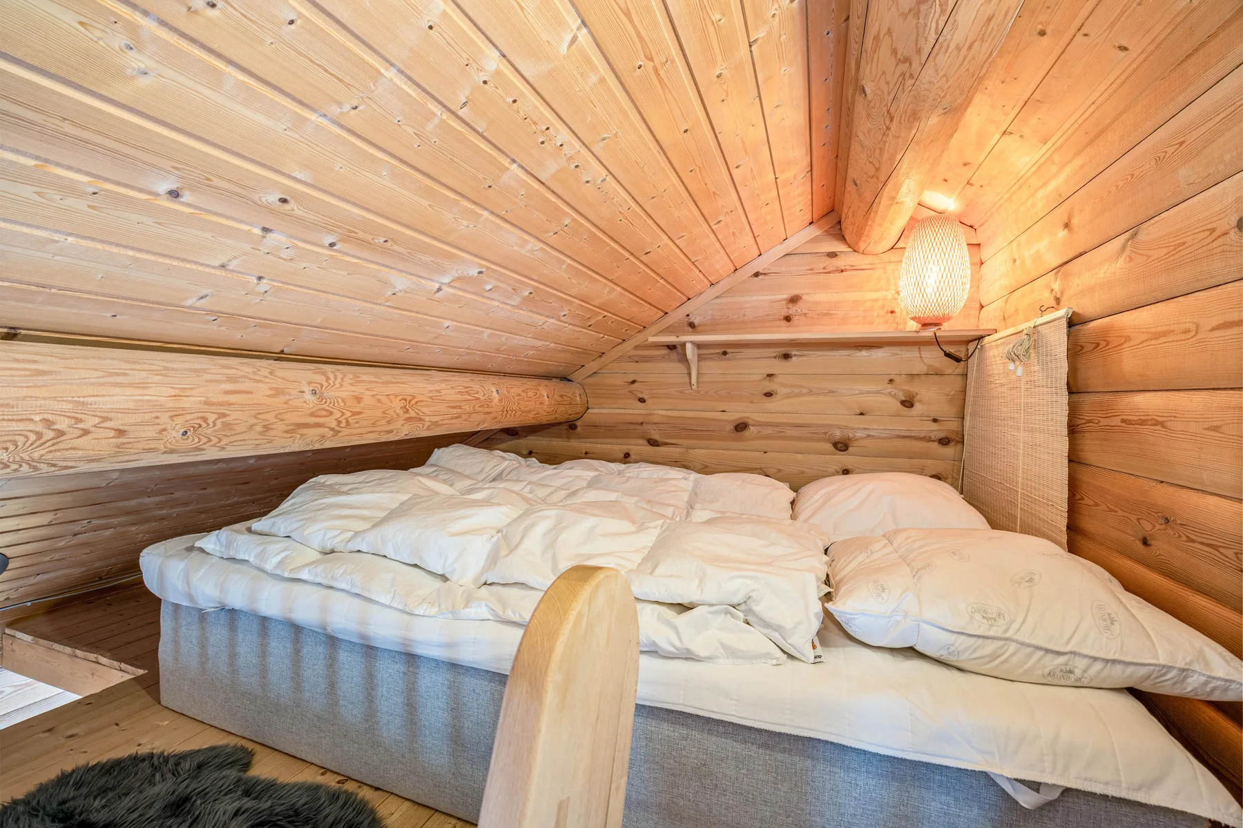 Zona para dormir de techo bajo, con una cama y revestimiento de madera cálido.