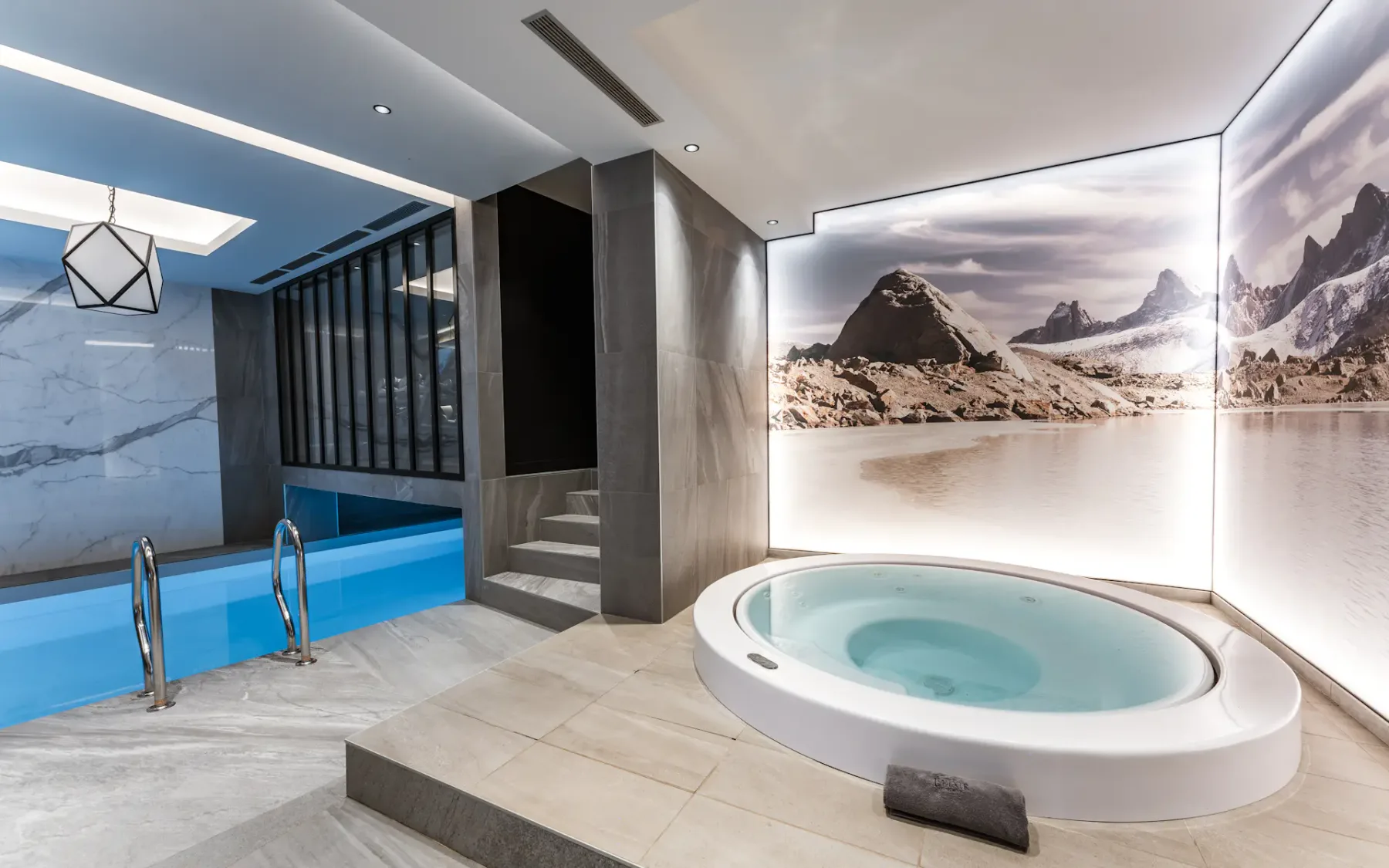 Luxurious indoor pool area with a hot tub, modern lighting, and a large mountain landscape mural on the wall.