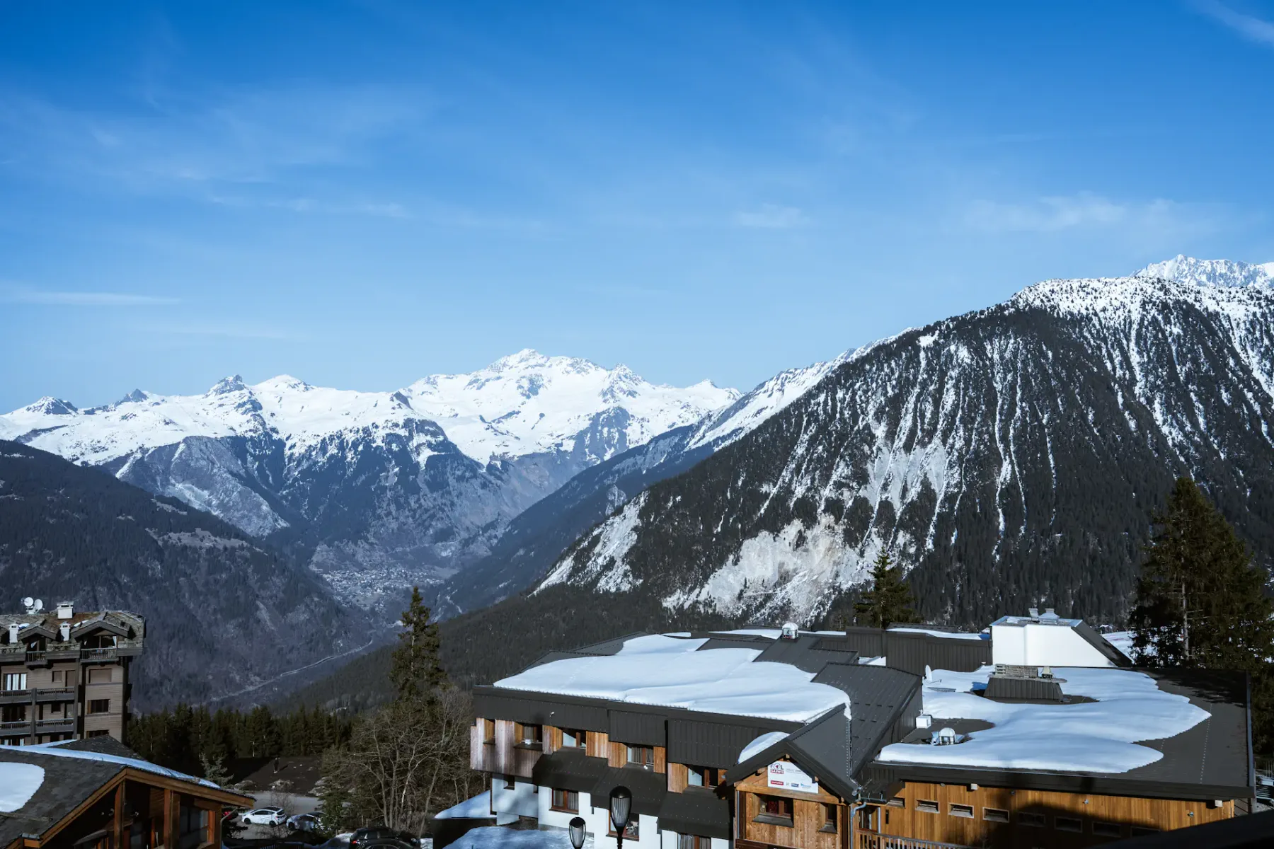 Snow-covered mountains under a clear blue sky, with wooden buildings in the foreground, creating a serene alpine landscape.