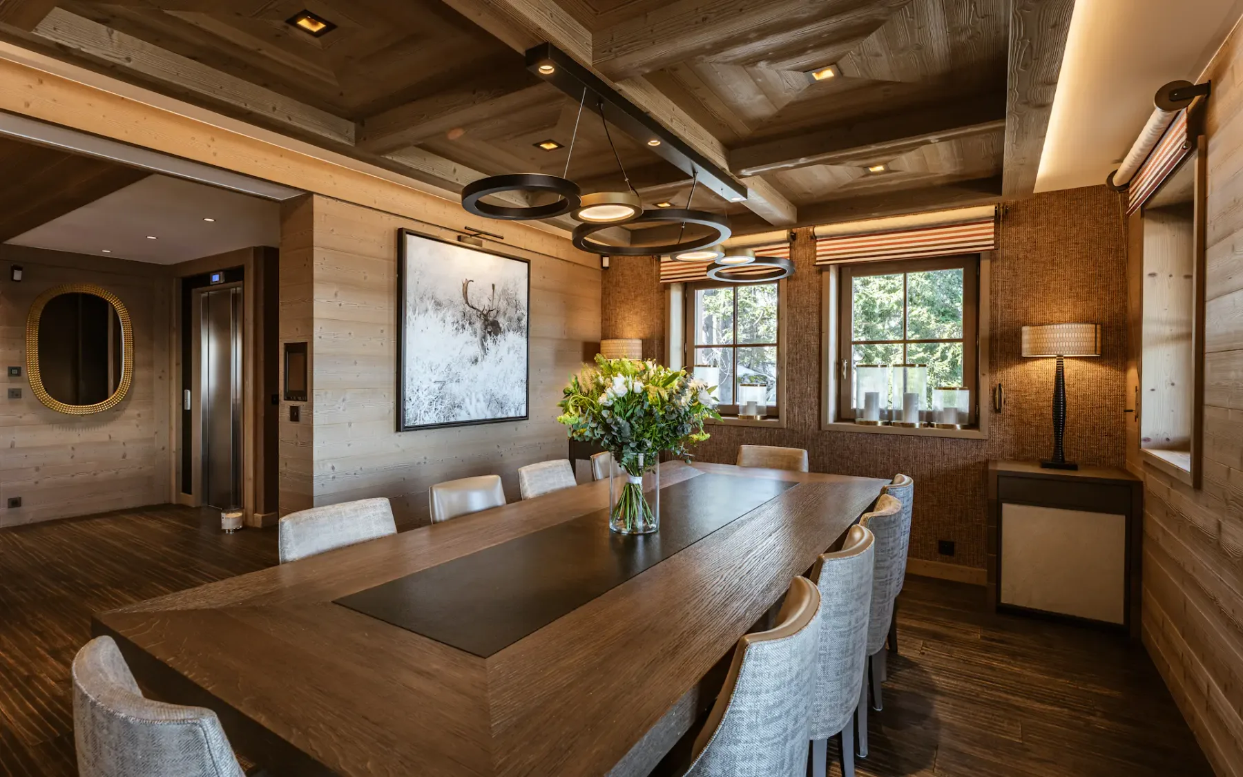 Elegant dining room with a large wooden table, modern chairs, floral centerpiece, artwork on the wall, and large windows with natural light.