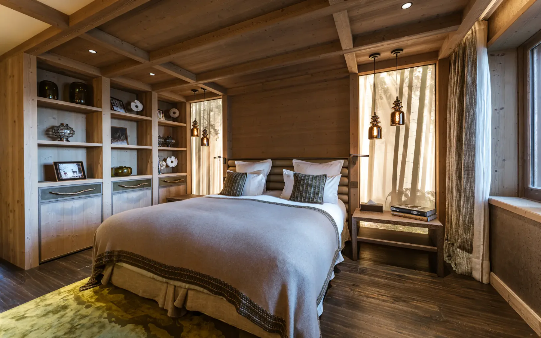 Cozy bedroom with wooden walls, a double bed, pendant lights, and a bookshelf. Large window with sheer curtains lets in natural light.