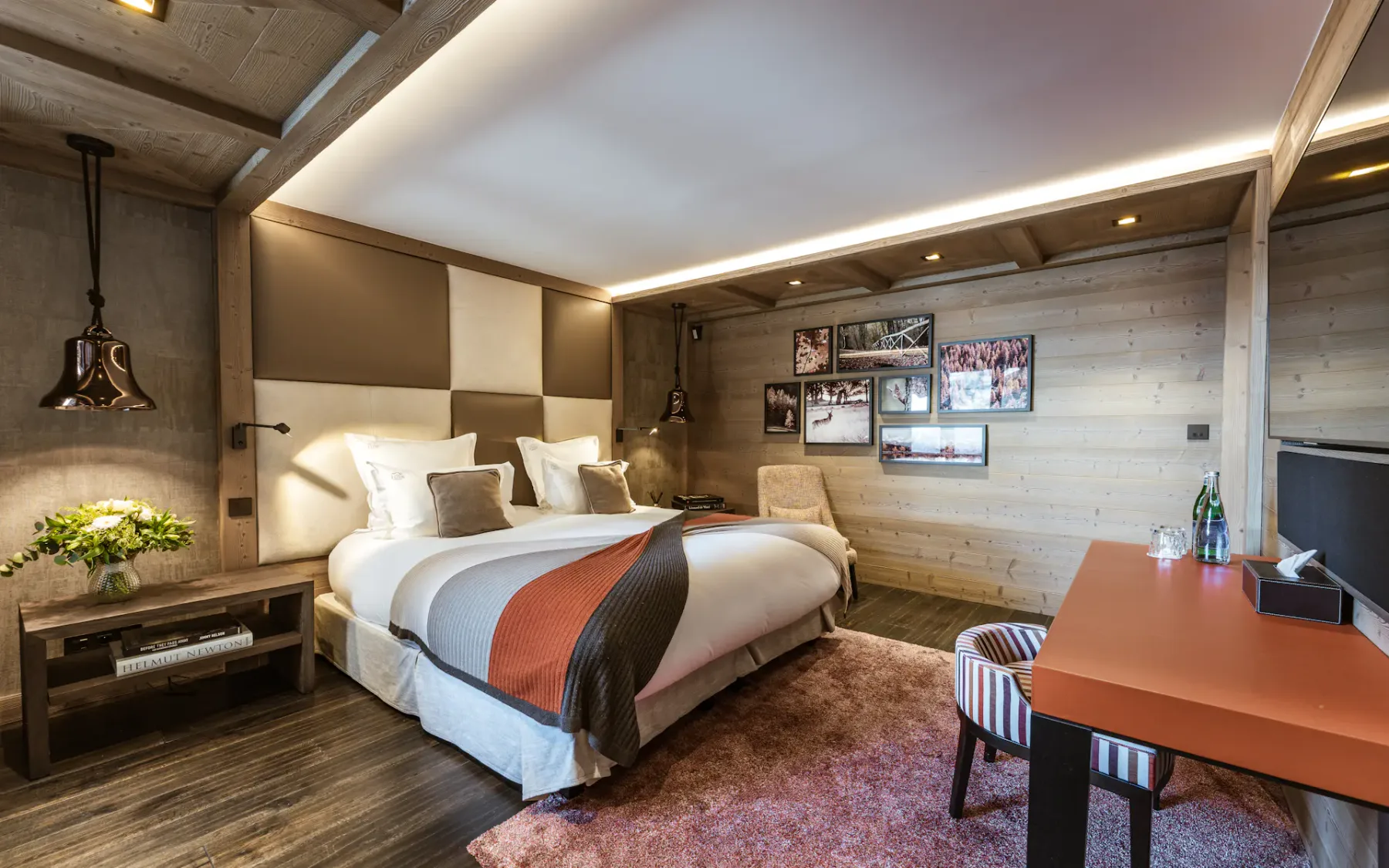 Cozy hotel room with a large bed, modern decor, soft lighting, a desk, and a plush rug. Walls feature wood paneling and framed photos.