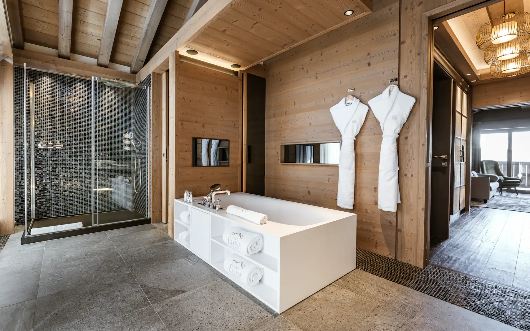 Luxurious bathroom with a wooden ceiling, a modern glass shower, a freestanding bathtub, and two white robes hanging on the wall.