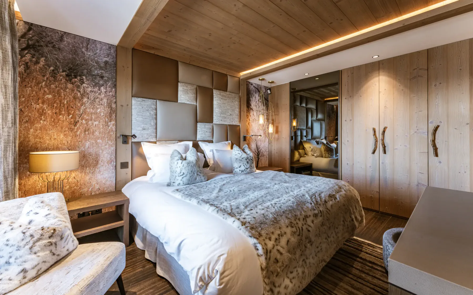 Cozy bedroom with a double bed, fur-patterned bedding, wooden walls, soft lighting, and a large mirror reflecting the room's decor.