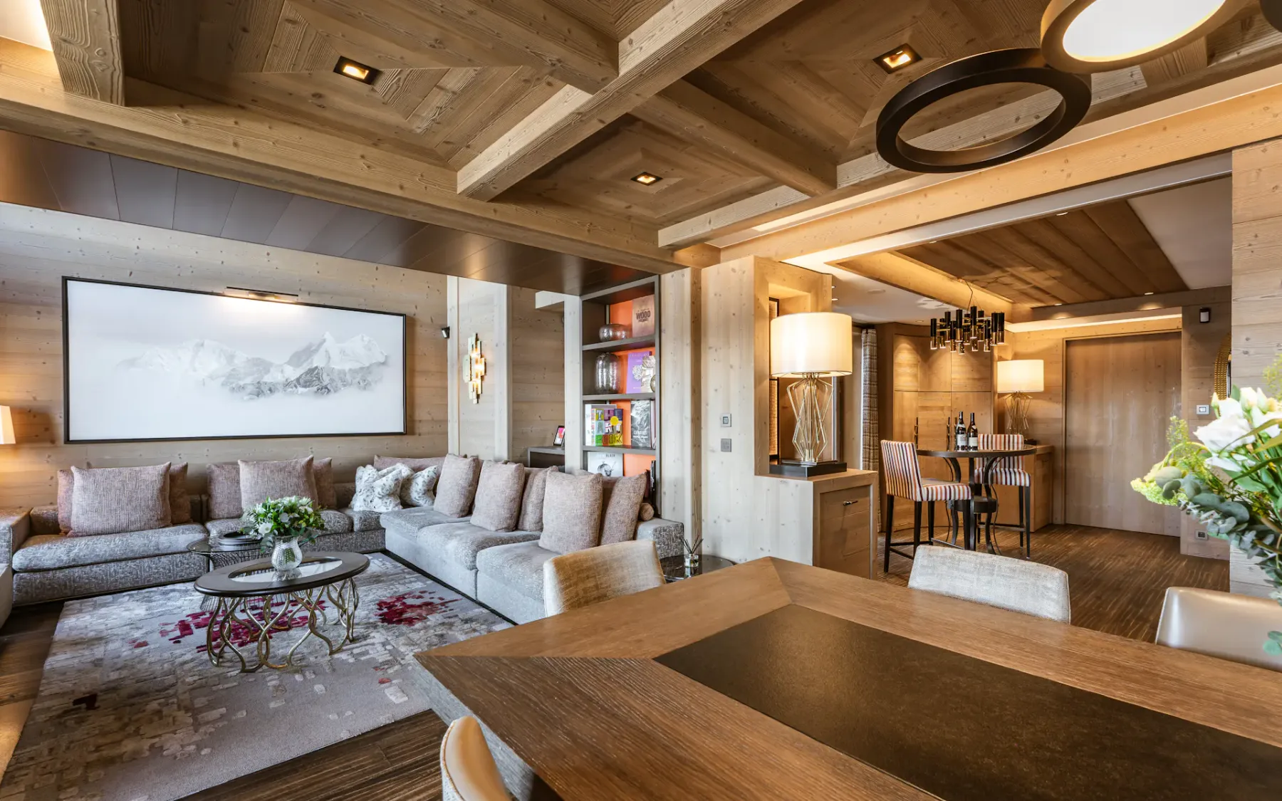 Cozy living and dining area with wooden interiors, modern furniture, a large sofa, wall art, and a dining table with chairs.