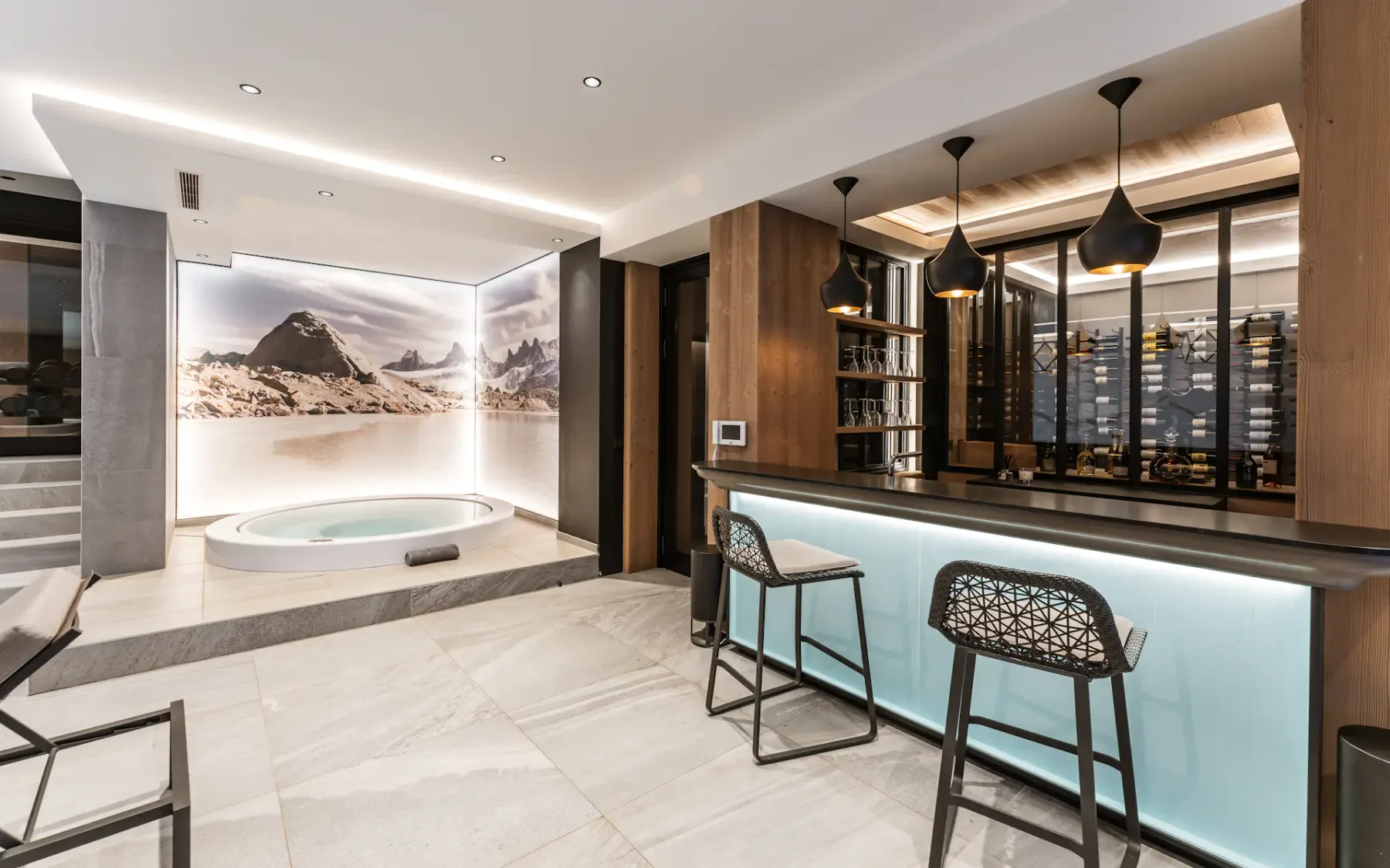 Modern room with a circular hot tub, sleek bar with high chairs, pendant lights, and a large mountain landscape mural on the wall.