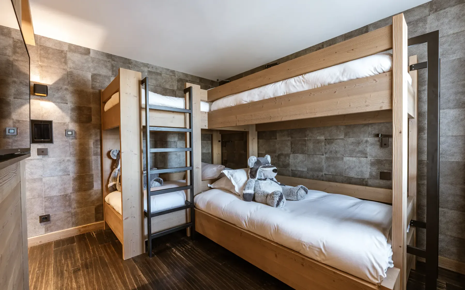 Wooden bunk beds in a cozy room with soft lighting, brown tiled walls, and neatly arranged towels on the lower bed.