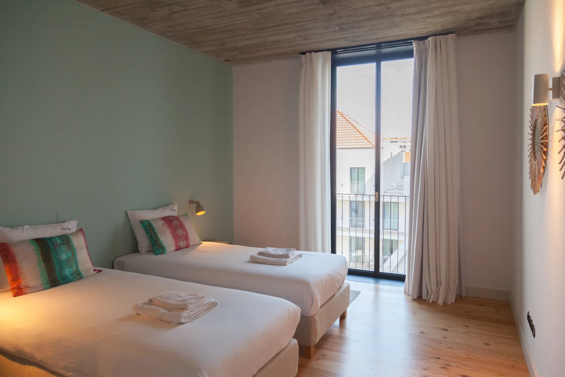A bedroom with two beds and a large window opening onto a balcony.