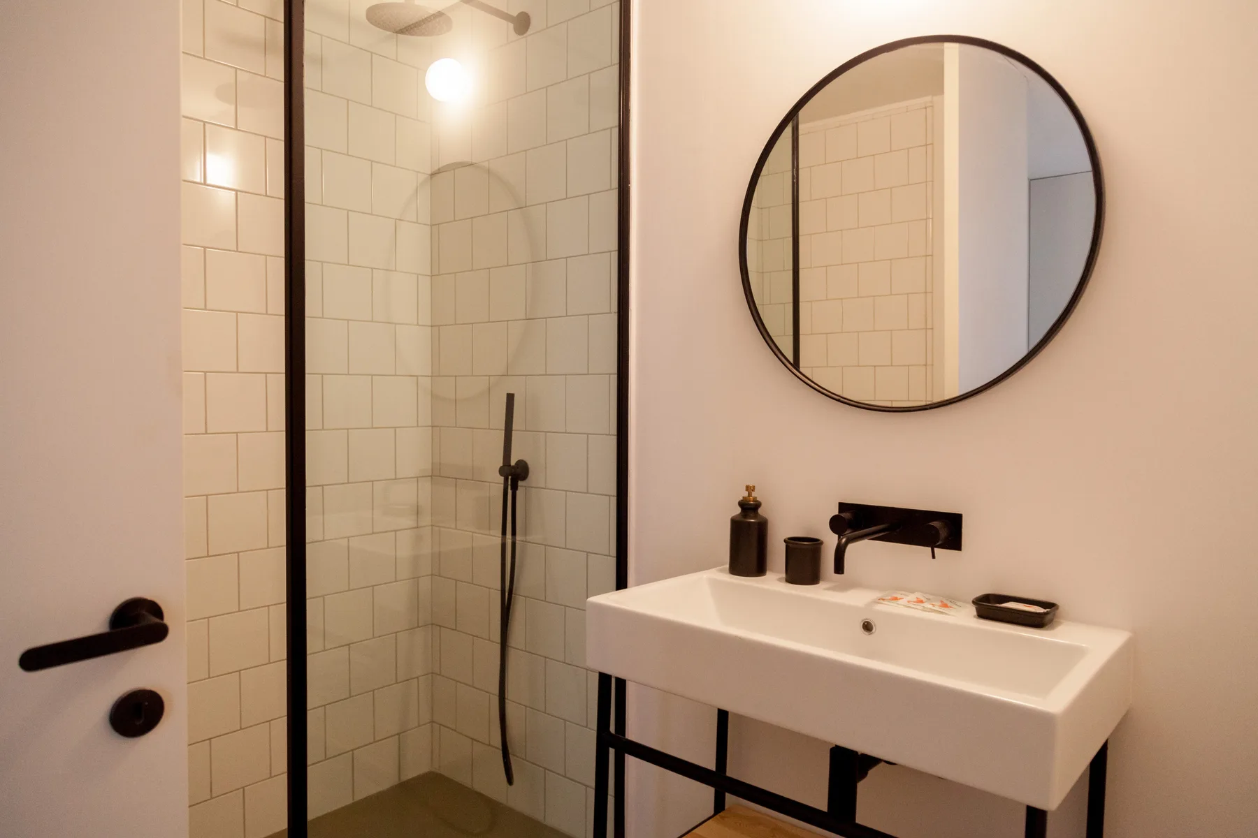 A bathroom with a tiled shower and a white sink beneath a round mirror.