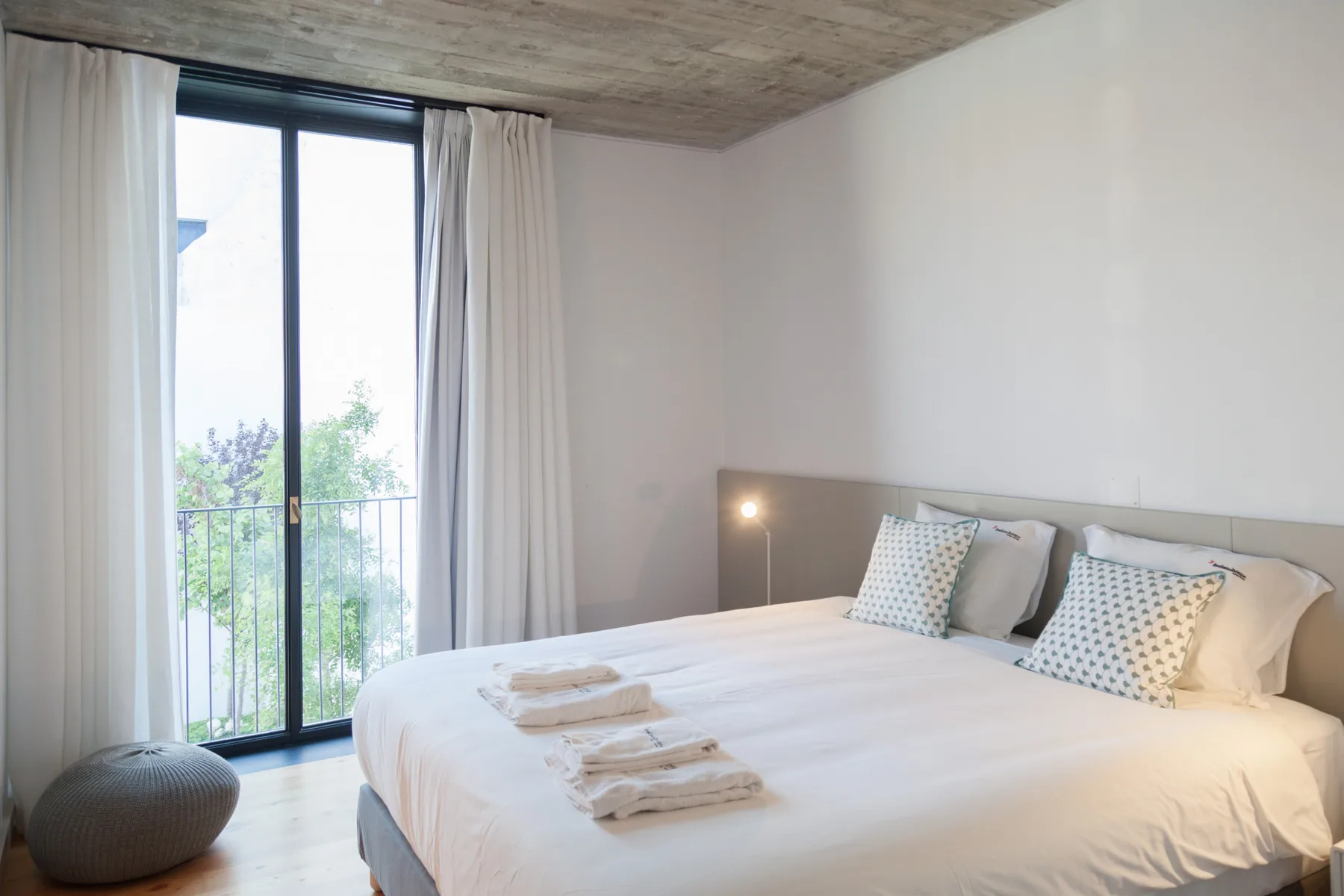 A bright bedroom with a neatly made bed and full-height windows.