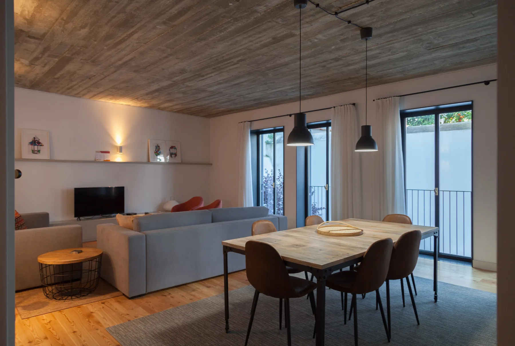 A dining and living area with a wooden table and seating beside large windows.