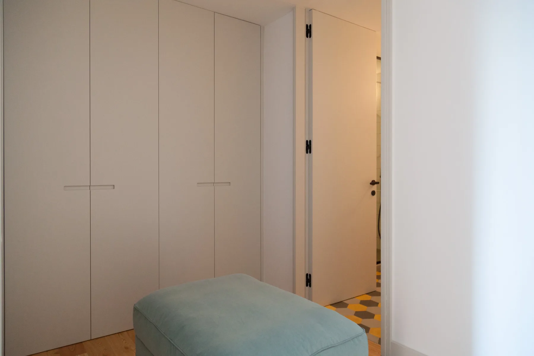 A bedroom area with built-in wardrobes and a cushioned bench beside an open doorway.