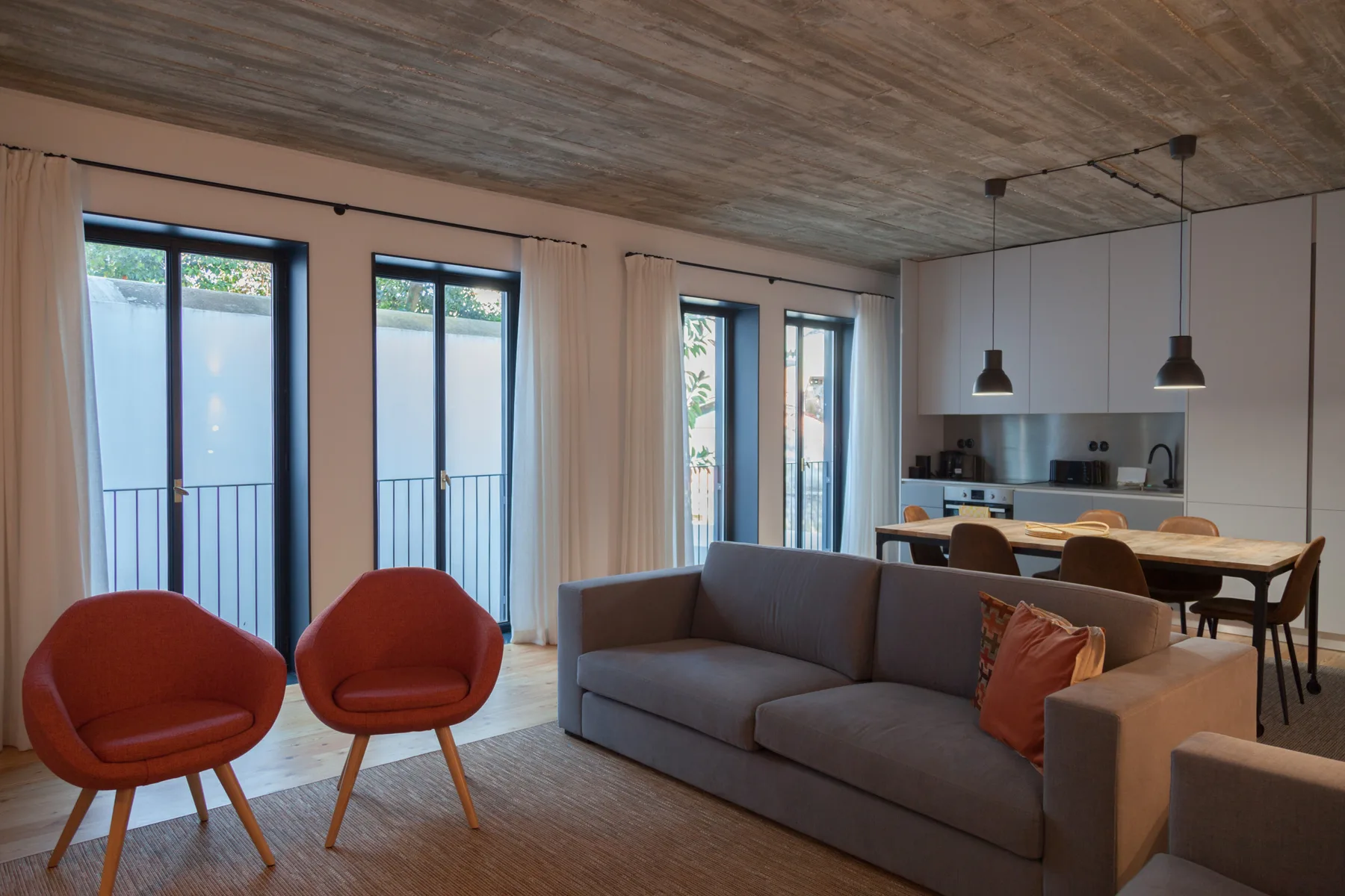A living and dining area with gray seating, red chairs, and a kitchen.