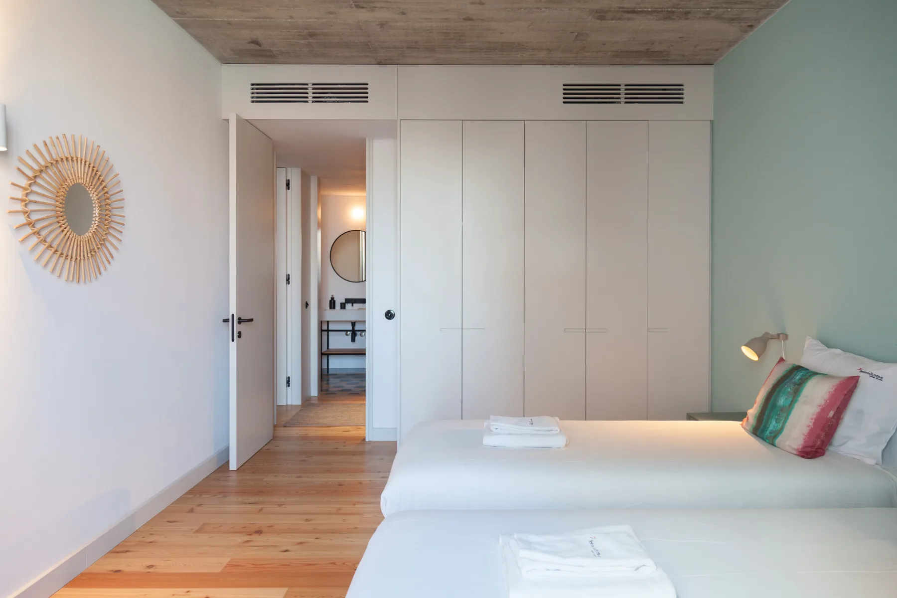 A bright bedroom with two beds, built-in wardrobes, and a wooden ceiling.