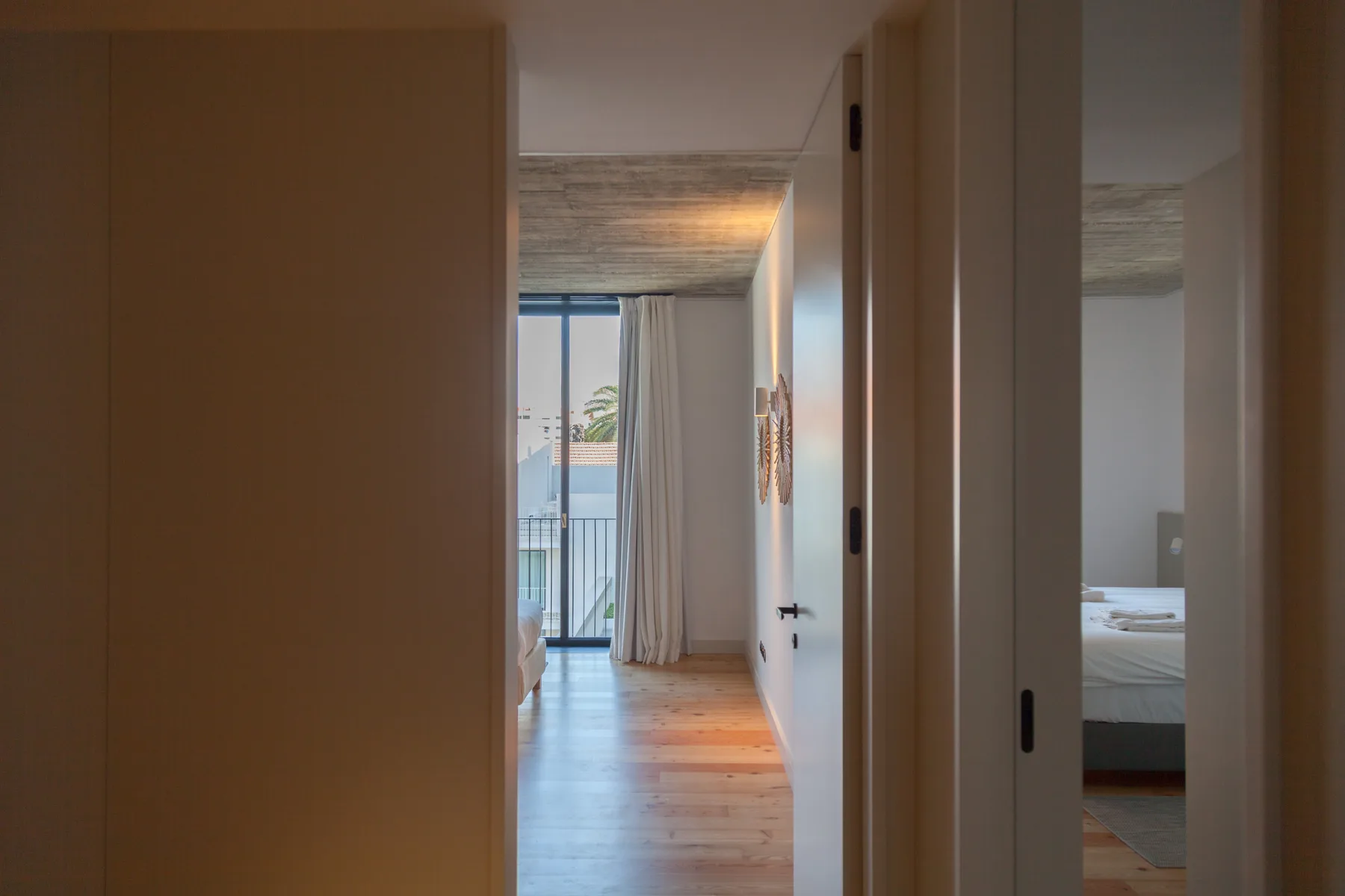 A bedroom doorway opens onto a hallway leading to a bright balcony.
