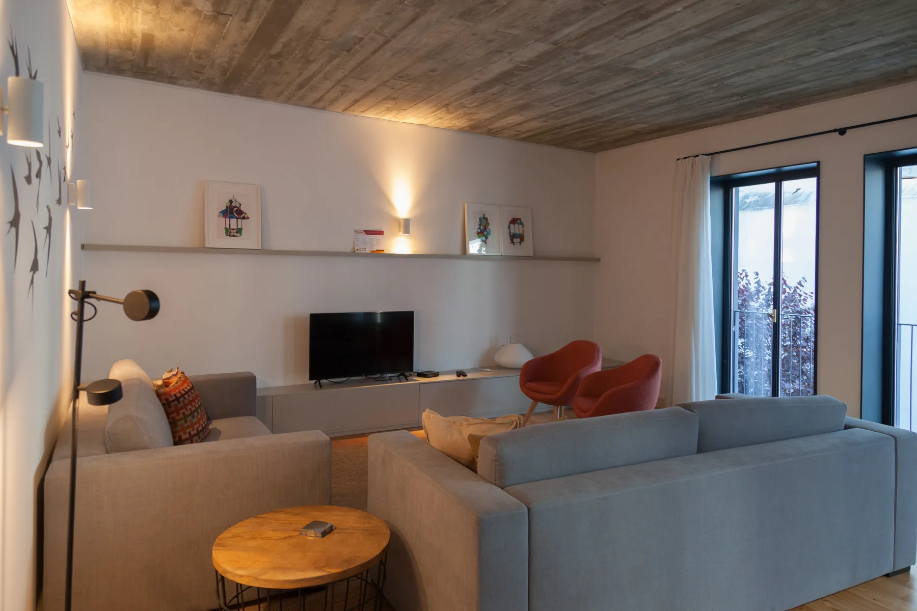 A living room with seating, a television, and large windows.