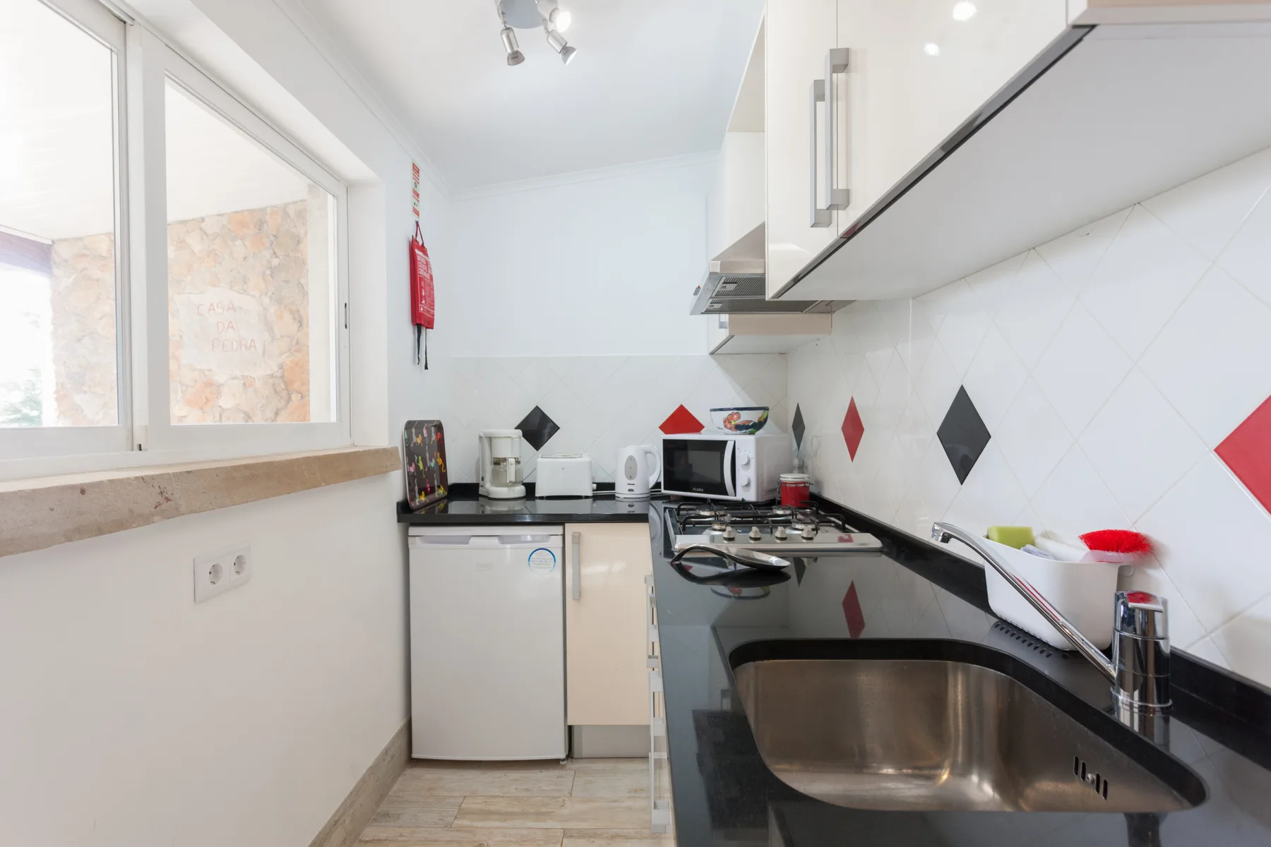 A bright kitchen with white cabinets, a window, and a stainless-steel sink.