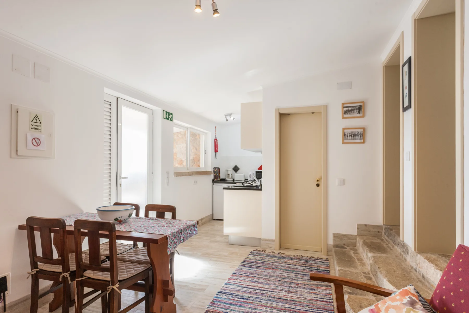 A dining area opens onto a compact kitchen, with a table and chairs beside a striped rug.