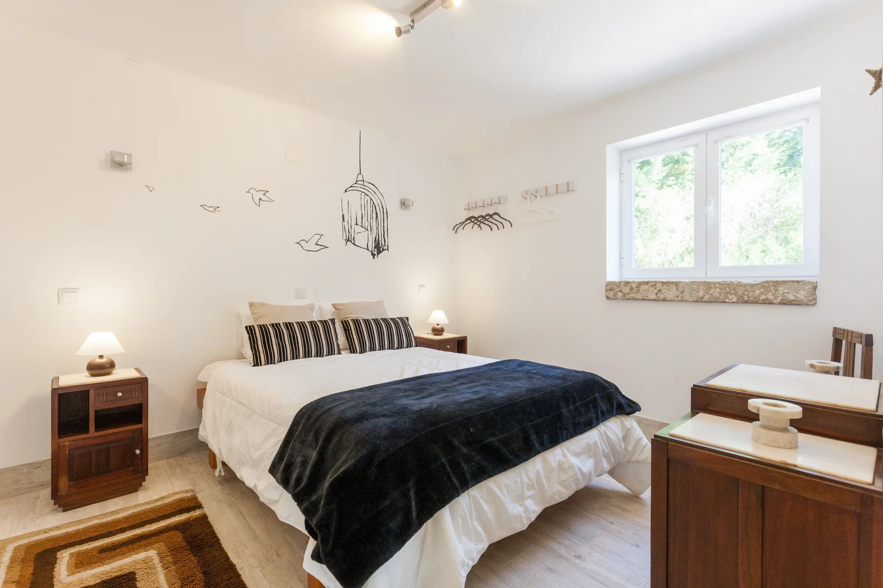 A bright bedroom with a double bed, dark bedding, and a window.