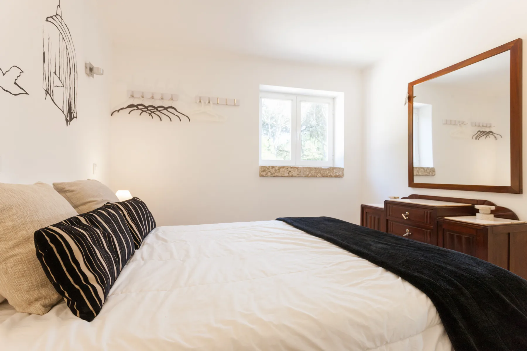 A bedroom with a bed, dark throw, and wooden dresser beneath a mirror.