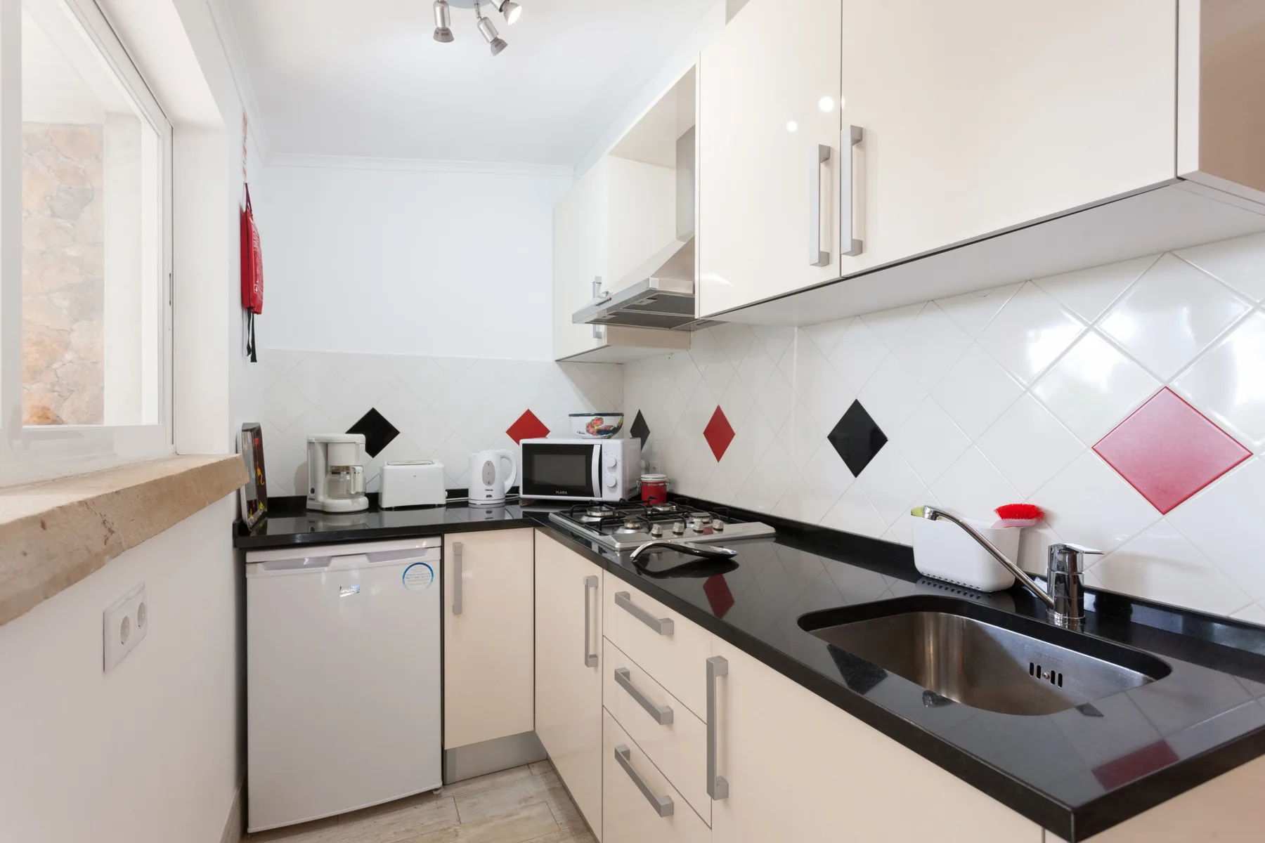 A bright kitchen with white cabinets, a tiled backsplash, and a black countertop.