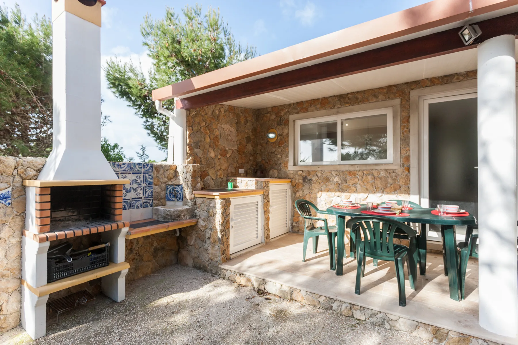 A covered outdoor dining area with a table beside a stone barbecue.