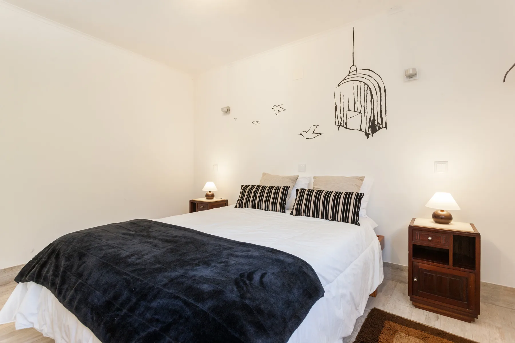 A bedroom with a bed, dark blanket, and matching bedside lamps.