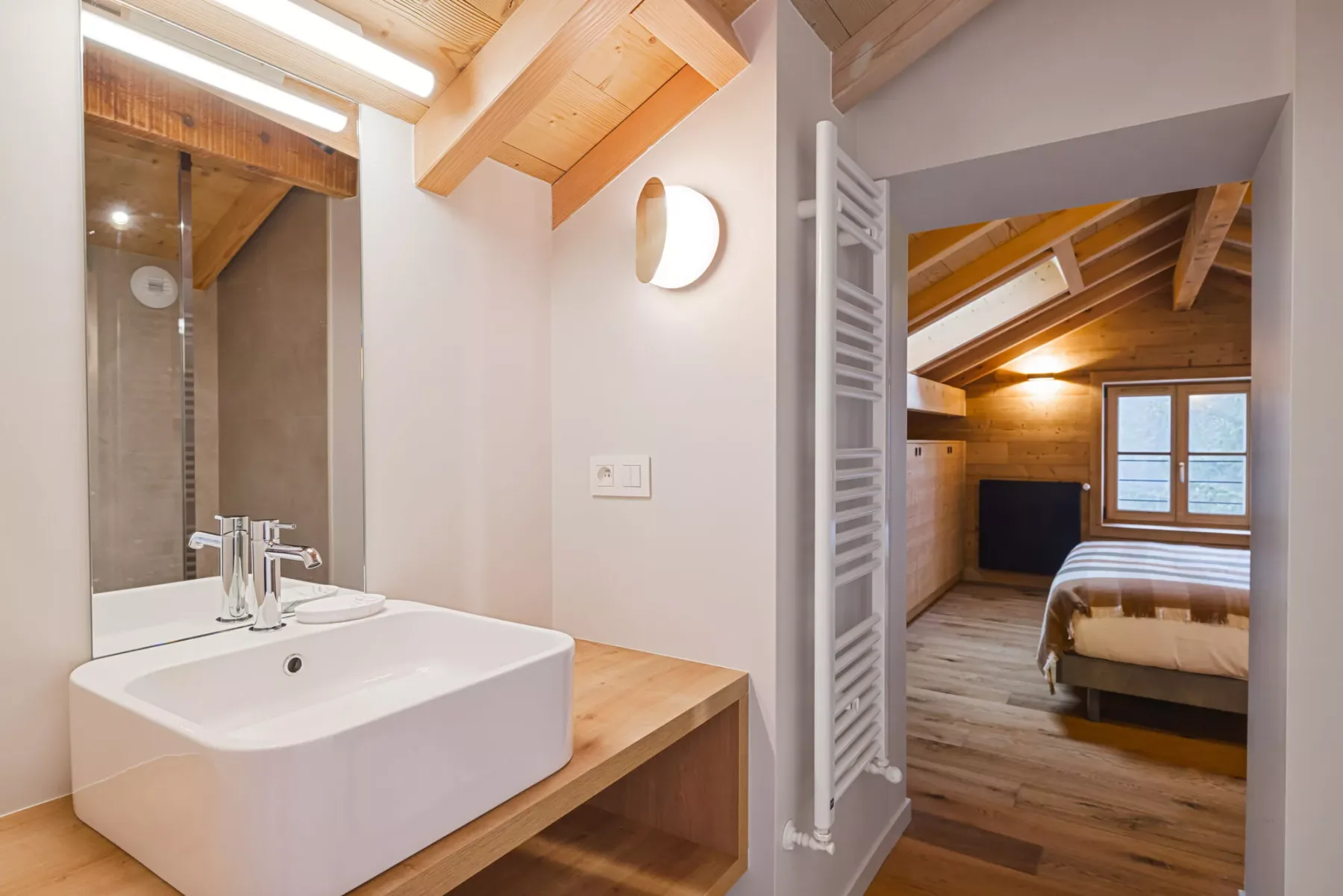 Un lavabo de baño da a un dormitorio con vigas de madera a la vista.