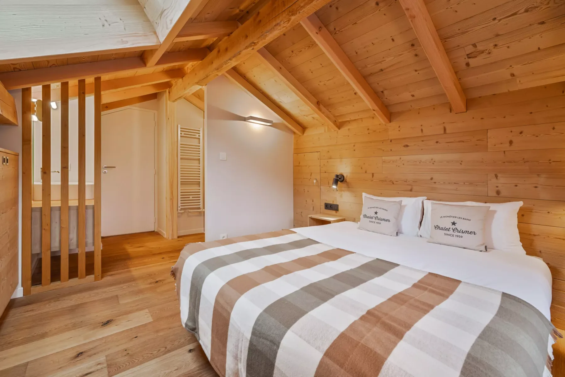 A wood-paneled bedroom with a bed beneath a sloped timber ceiling.
