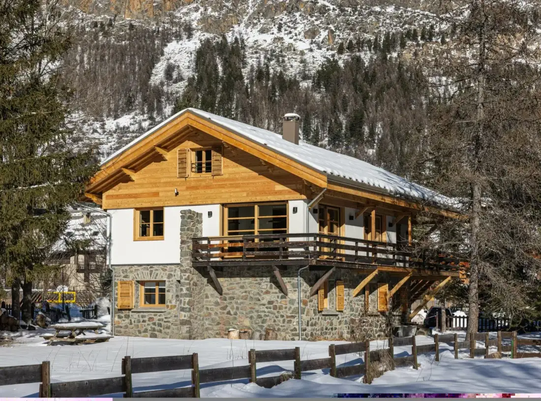 A chalet with wooden balconies stands in a snowy mountain setting.