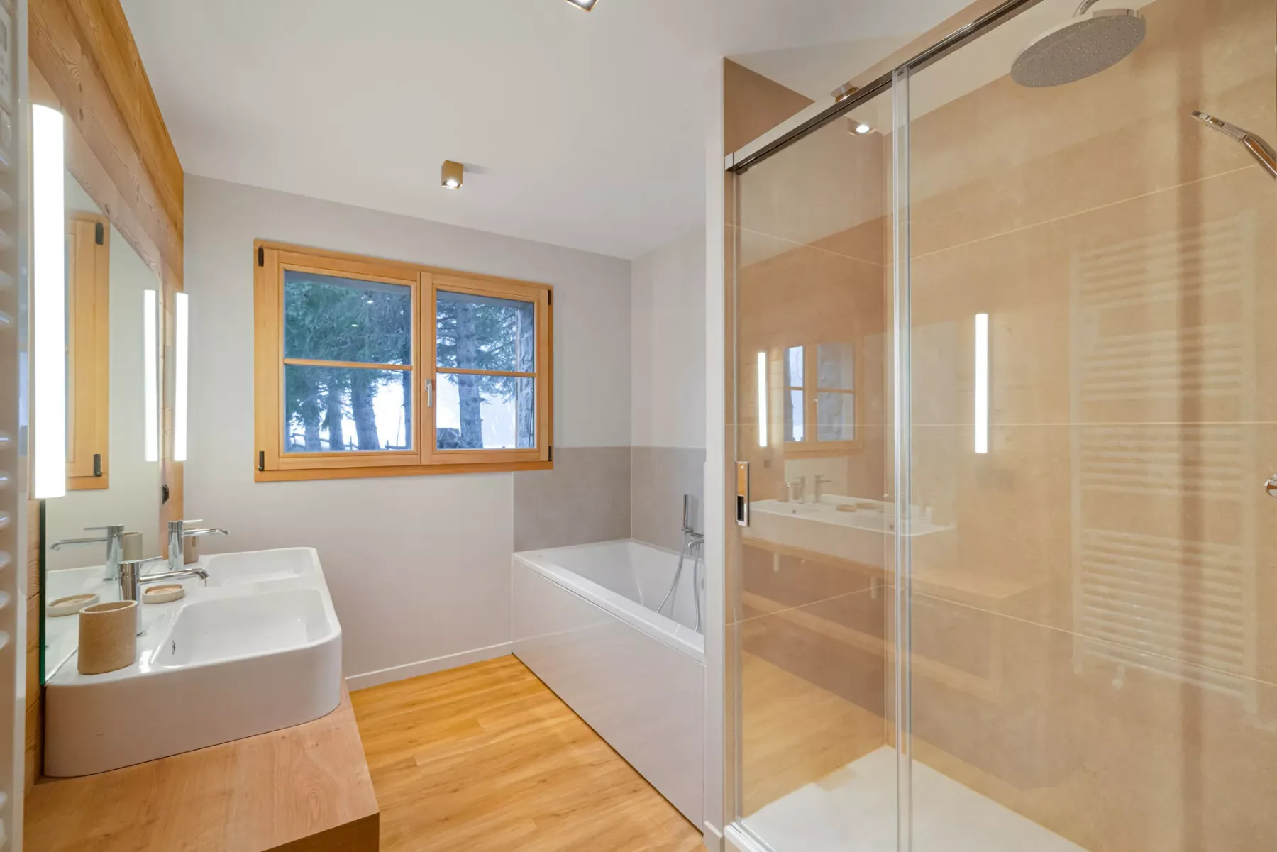 A bright bathroom with a bathtub, glass shower, and wood-framed window.
