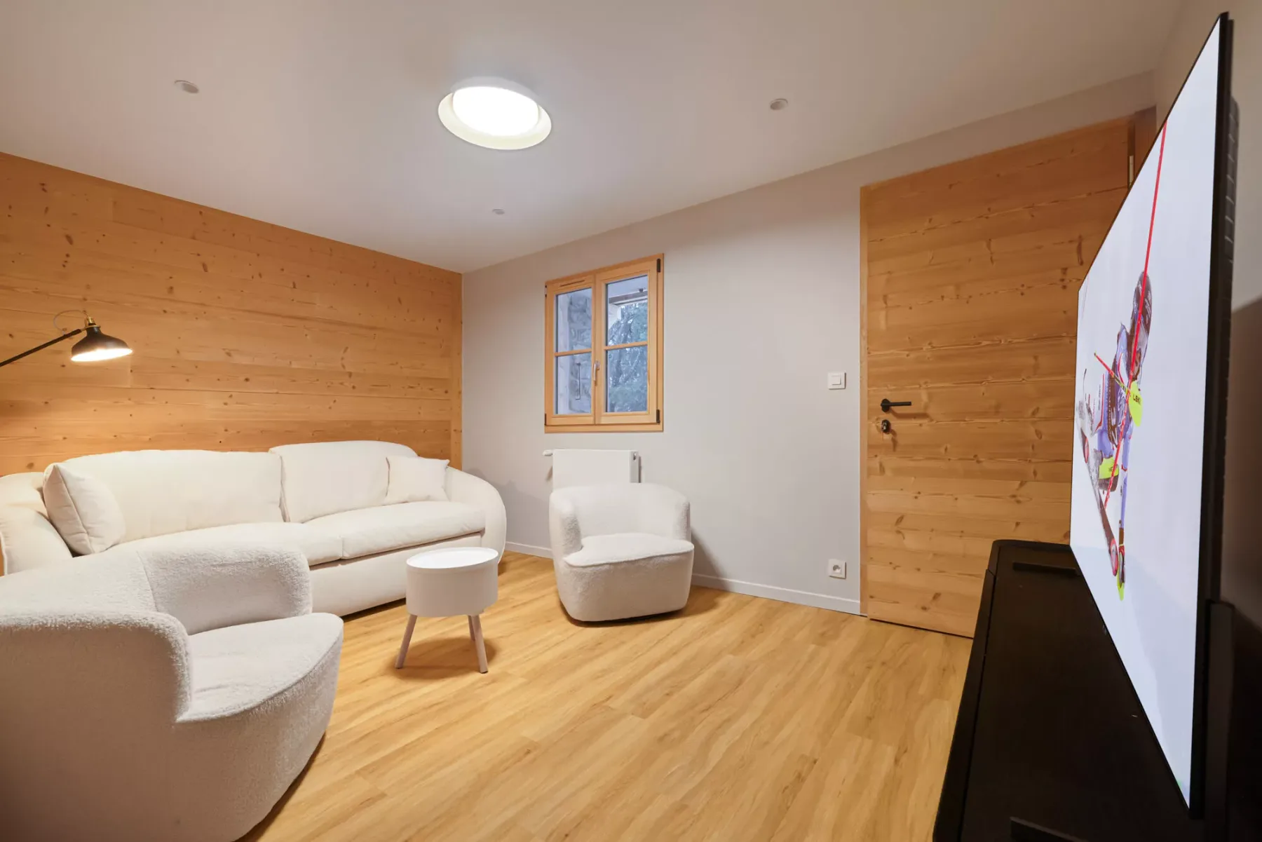 Una sala de estar con asientos claros, paredes revestidas de madera y un televisor.