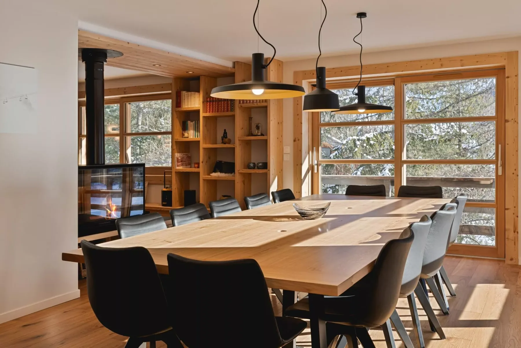 A dining area with a long wooden table and large windows.